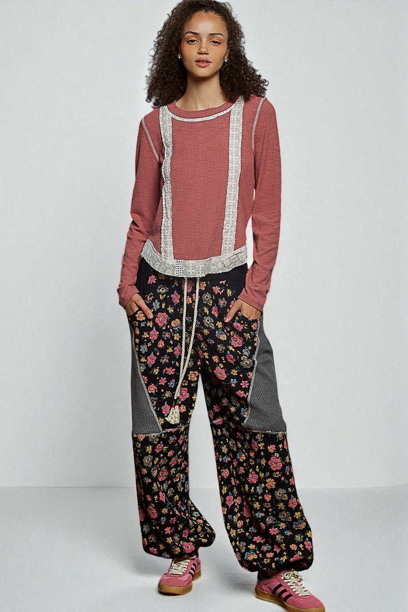 Woman wearing a pink long-sleeve top and floral pants on a white background