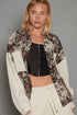 Woman wearing a floral jacket over a black top and white pants on a gray background