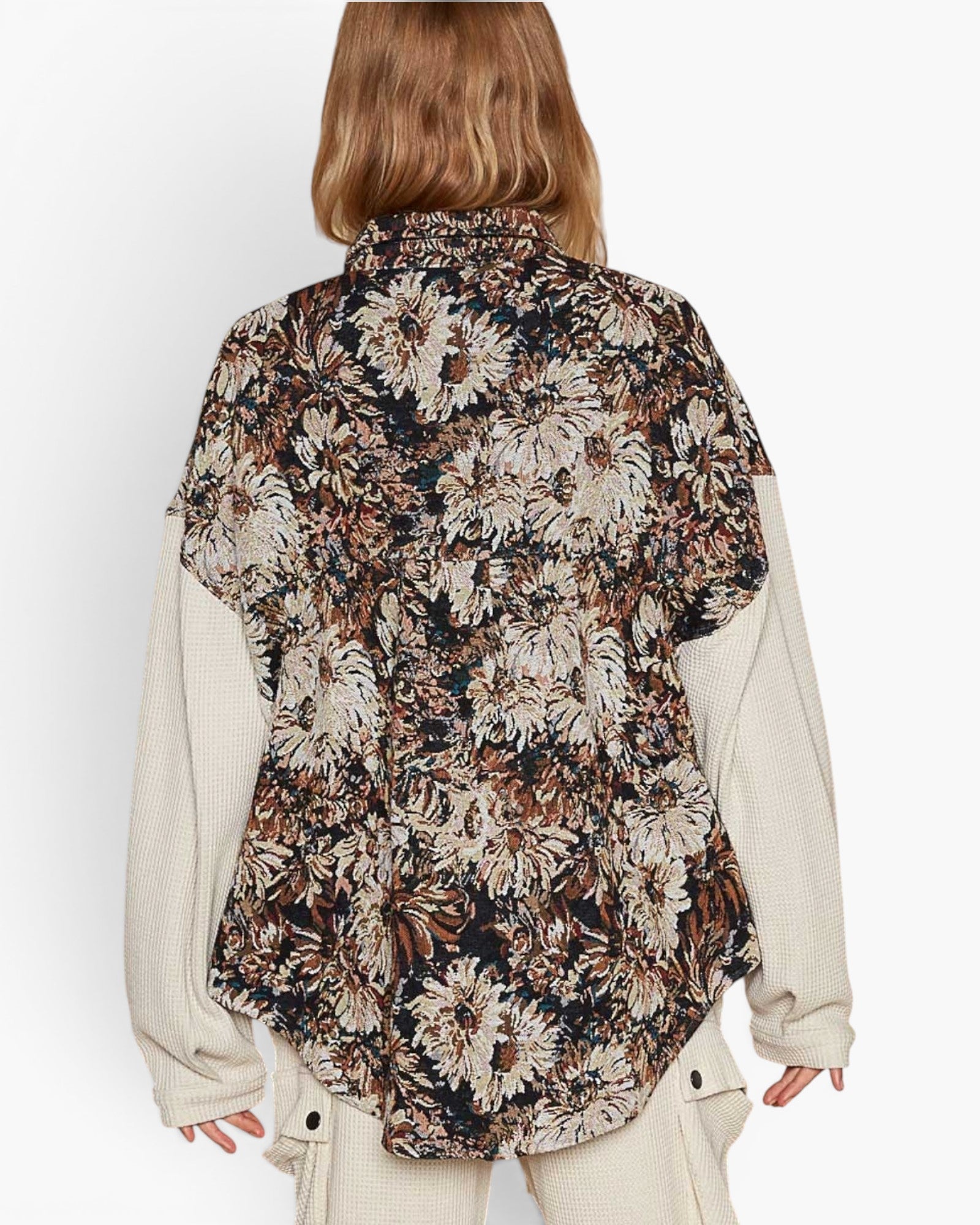 A model shown from the back wearing a short-sleeve button-up shirt with a dense floral print in beige, brown, and black, layered over a cream ribbed knit long-sleeve shirt.