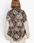 A model shown from the back wearing a short-sleeve button-up shirt with a dense floral print in beige, brown, and black, layered over a cream ribbed knit long-sleeve shirt.