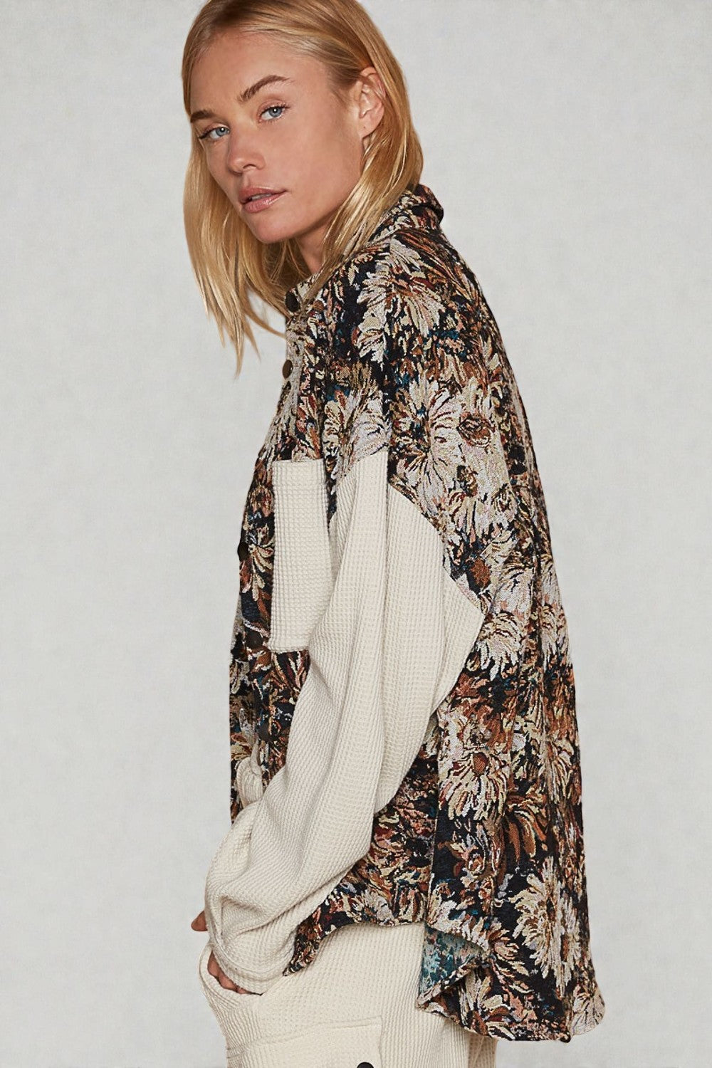 Woman wearing a floral kimono-style garment over a white sweater on a plain background