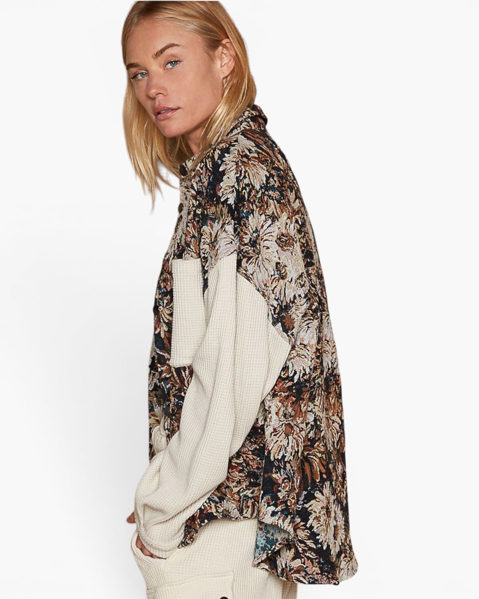 A woman shown in side profile wearing a long-sleeve button-up shirt with a dark floral and botanical print over a cream ribbed knit sweater, set against a plain white studio background.