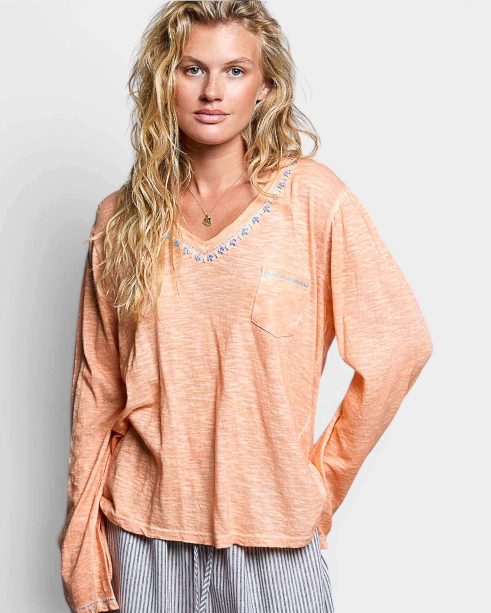Woman wearing a peach-colored long-sleeve top with decorative trim on a light gray background