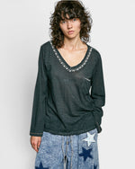 Person wearing a black long-sleeve top with decorative trim on a plain background