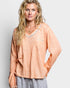 Woman wearing a peach-colored long-sleeve top with decorative trim on a light gray background