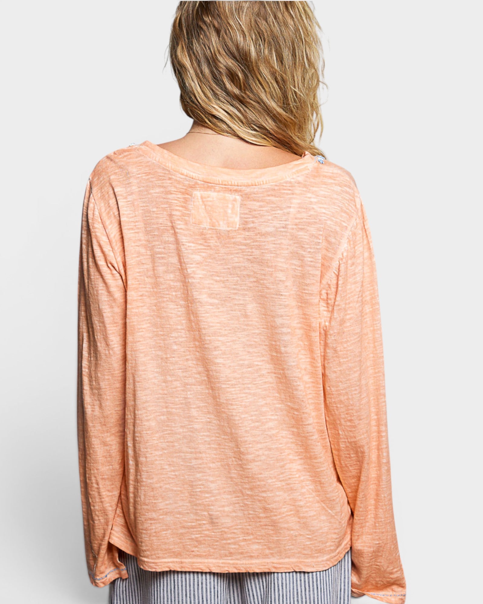 Woman wearing a peach-colored long-sleeve top on a white background