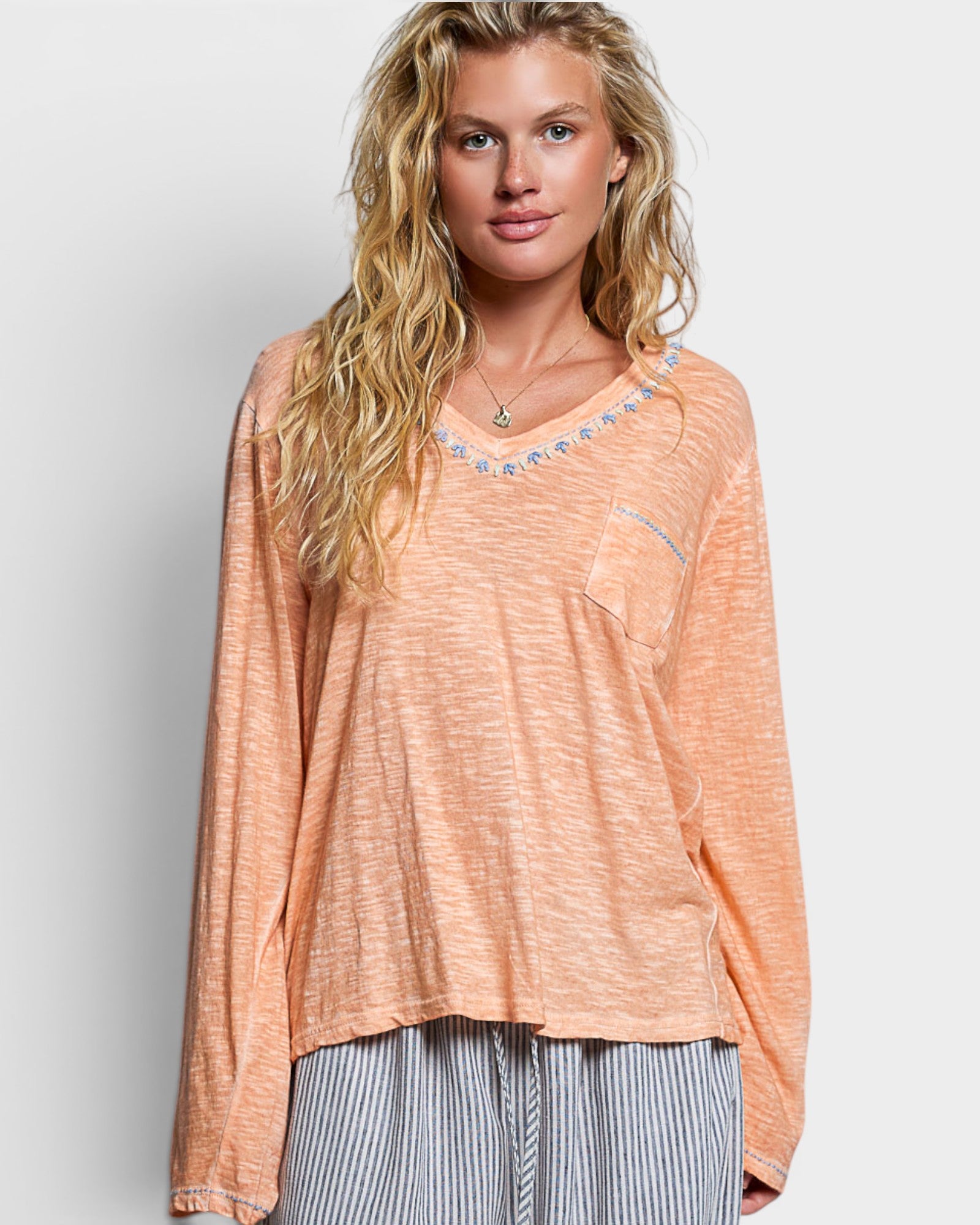 Woman wearing a peach-colored long-sleeve top with a subtle pattern on a plain background