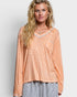Woman wearing a peach-colored long-sleeve top with a subtle pattern on a plain background