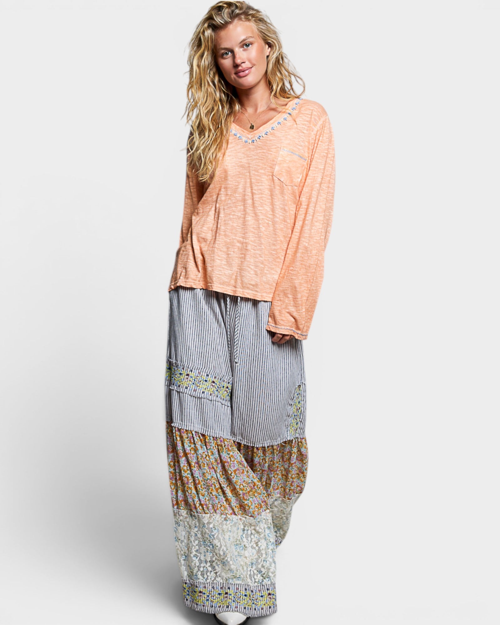 Woman wearing a peach top and patterned long skirt on a white background