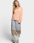 Woman wearing a peach top and patterned long skirt on a white background