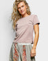 Woman wearing a mauve t-shirt and patterned pants against a plain background