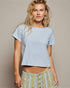 Woman wearing a light blue t-shirt and patterned pants against a neutral background