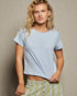Woman wearing a light blue t-shirt and patterned pants against a beige background