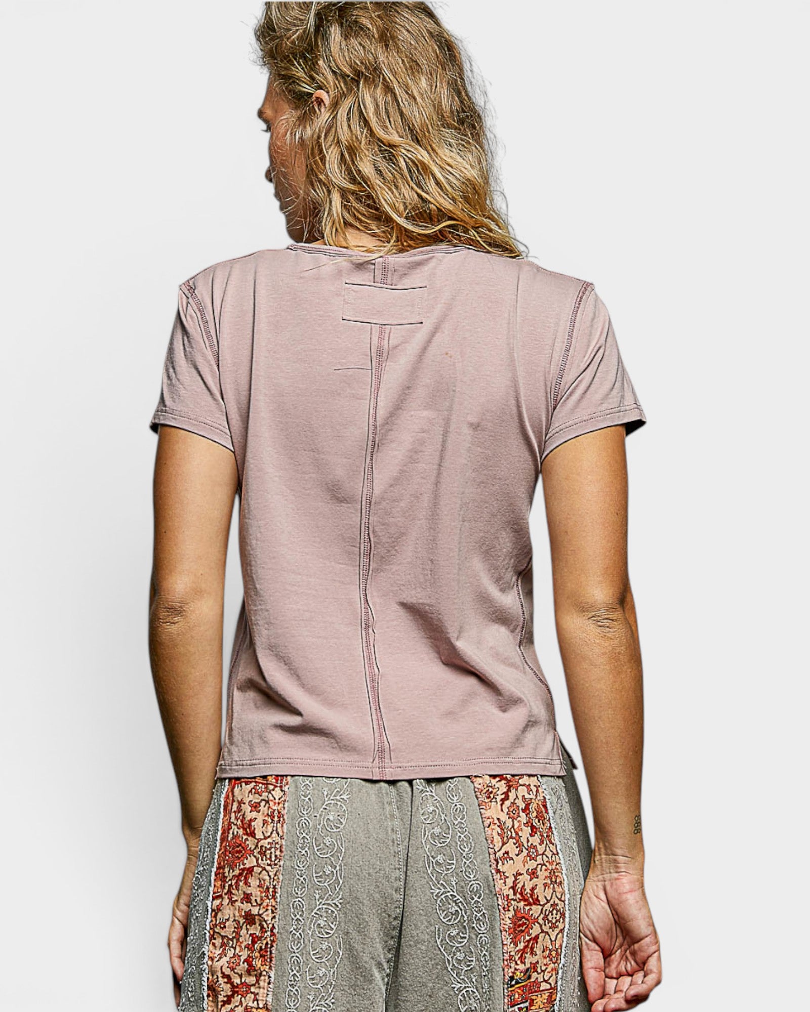Person wearing a mauve t-shirt with a floral pattern on the bottom half of the pants against a white background