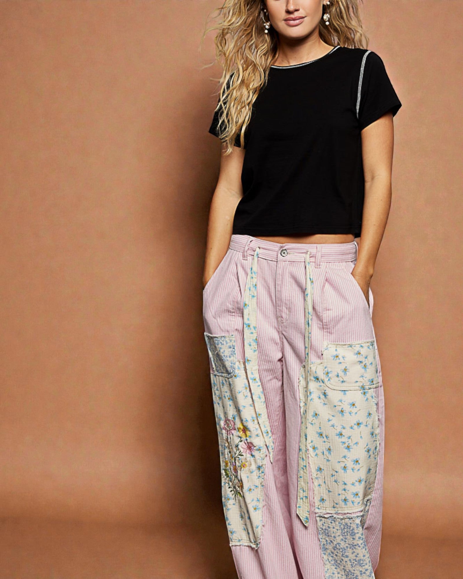 Woman wearing a black top and floral patchwork pants against a brown background