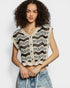Woman wearing a black and white patterned sleeveless top with denim shorts on a plain background