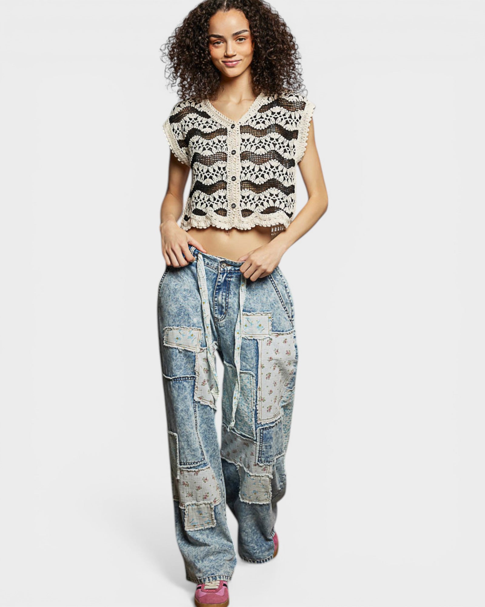 Woman wearing a crochet top and patchwork jeans on a white background