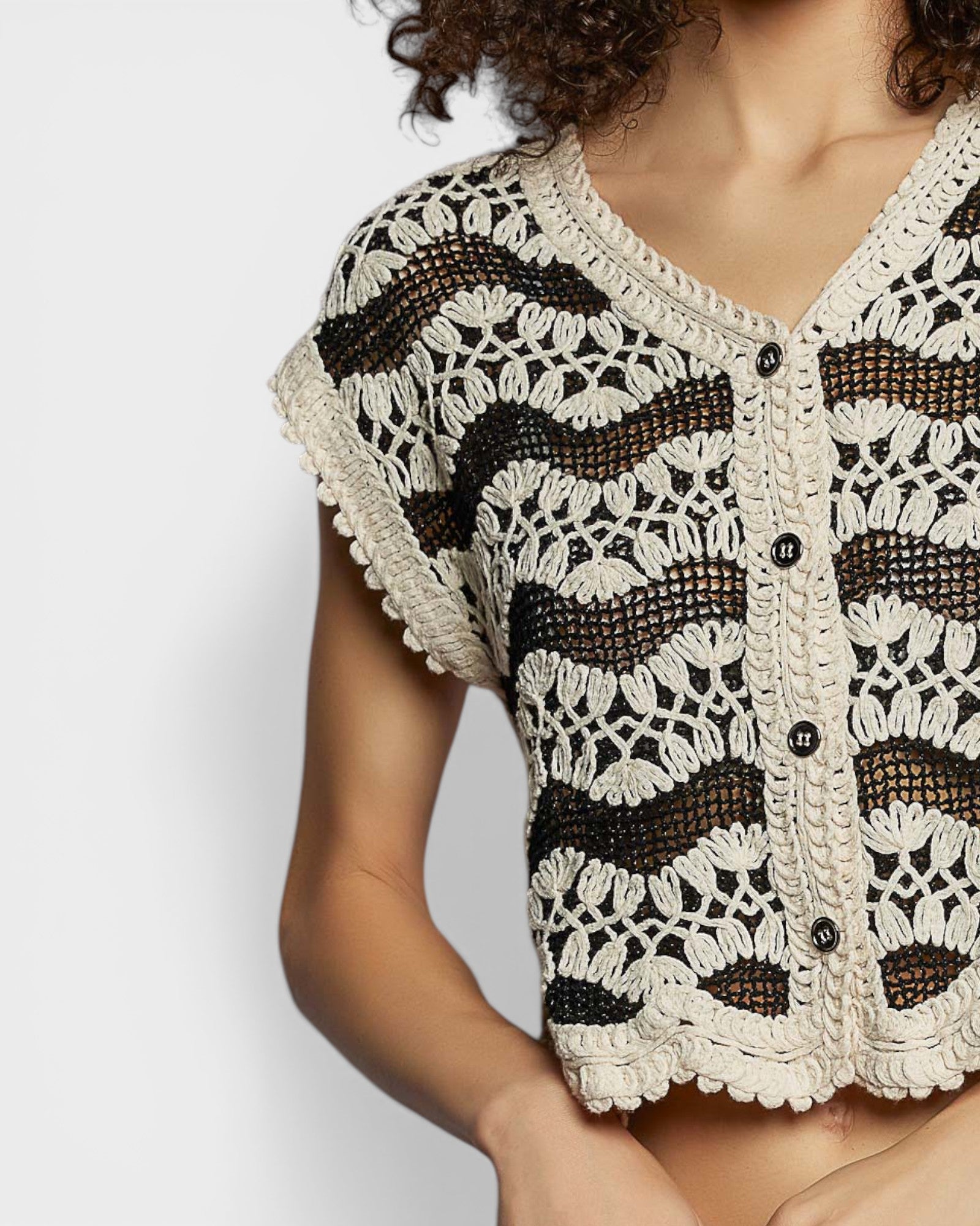 Woman wearing a black and white crochet cardigan on a light gray background