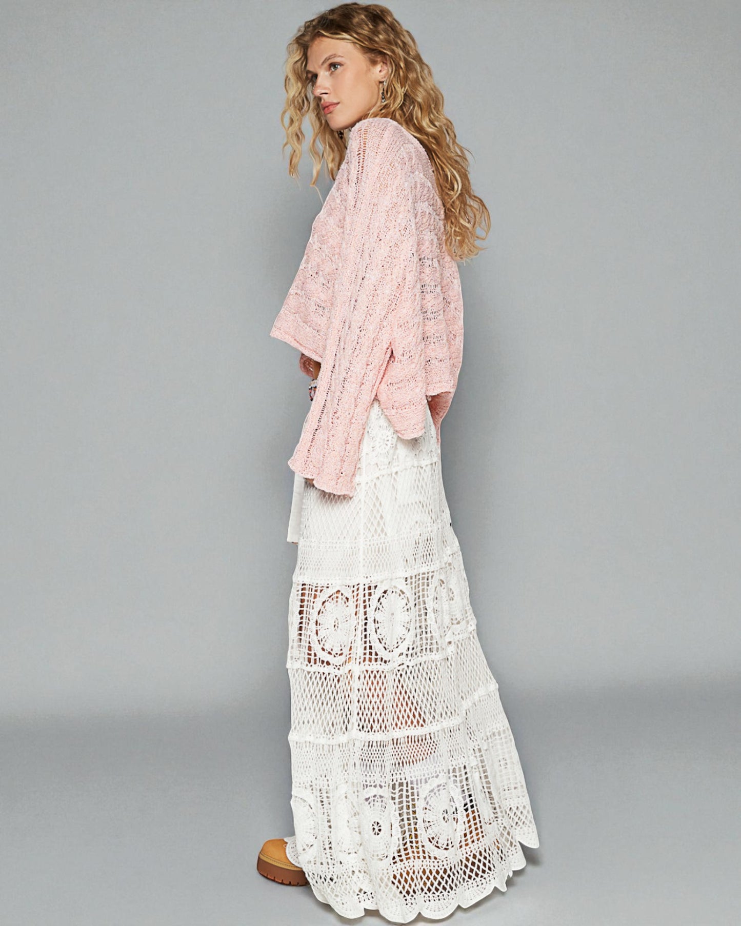 Woman wearing a pink lace top and white lace skirt on a gray background