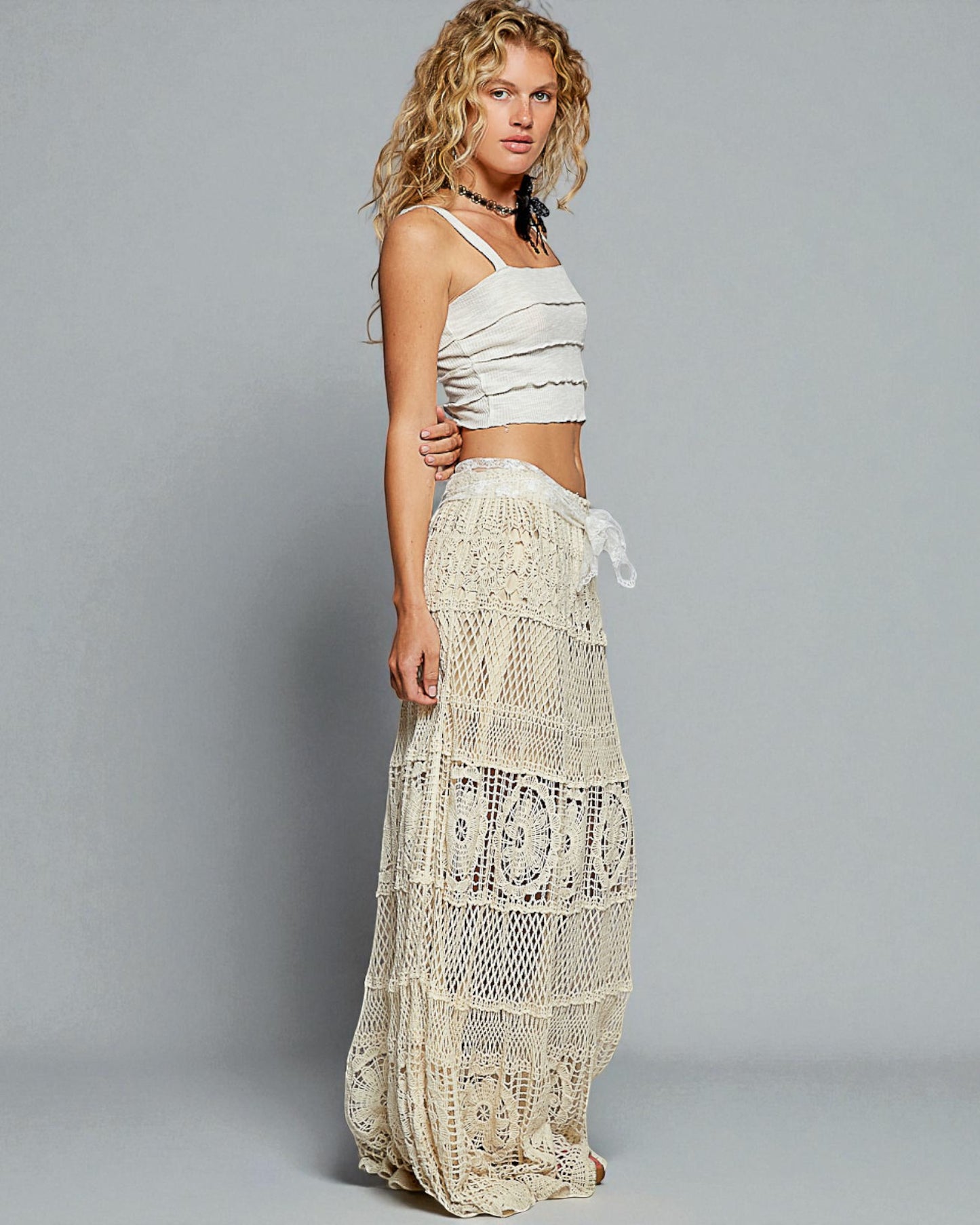 Woman wearing a white crochet skirt and top against a gray background