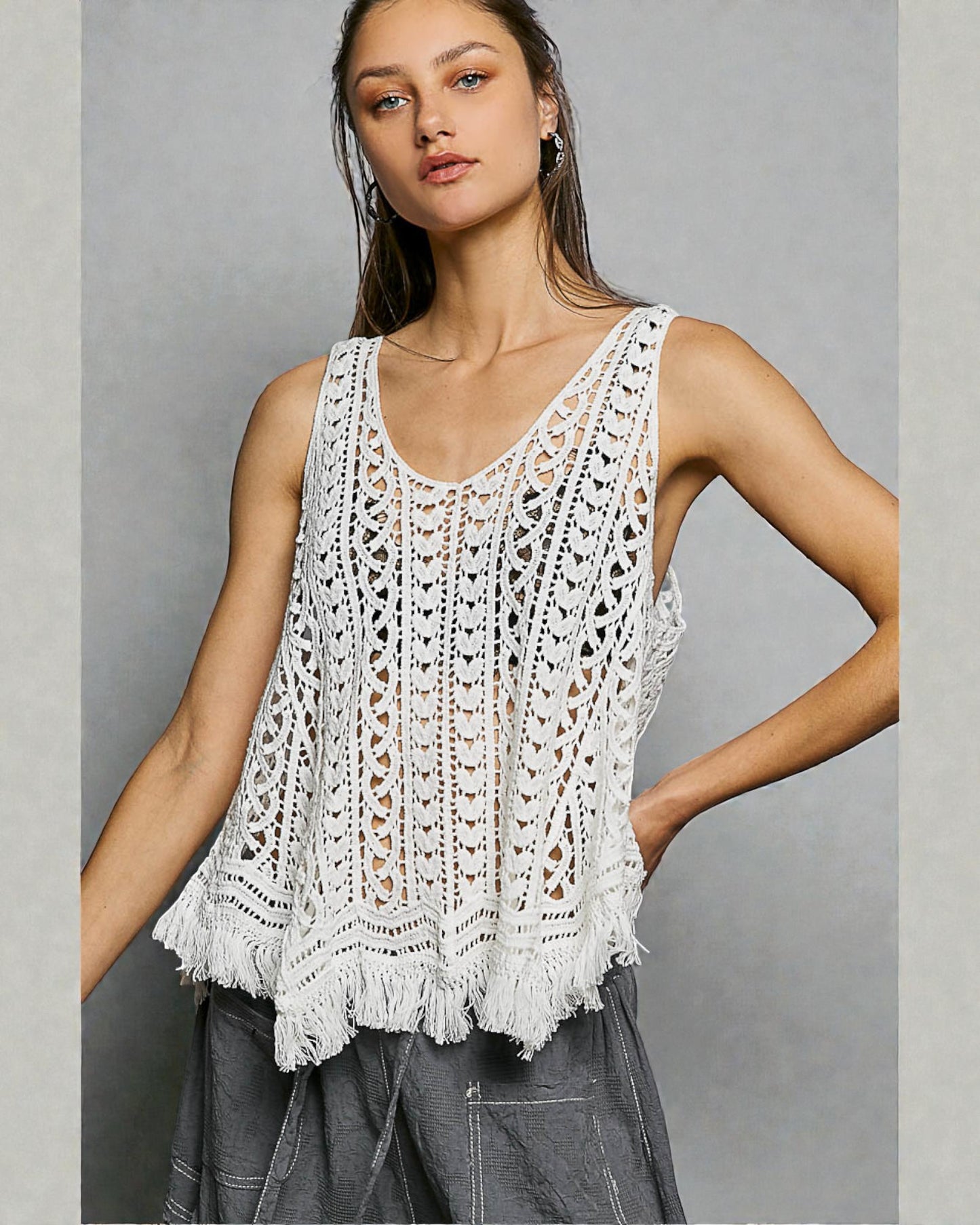 Woman wearing a white crochet tank top against a gray background