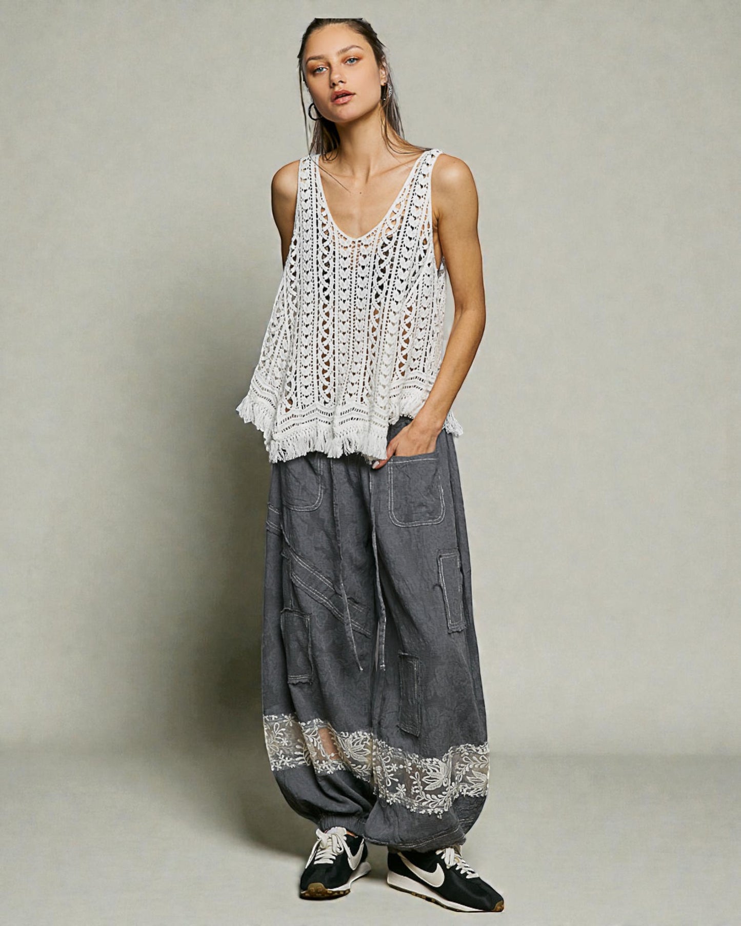 Woman wearing a white crochet top and gray wide-leg pants against a plain background