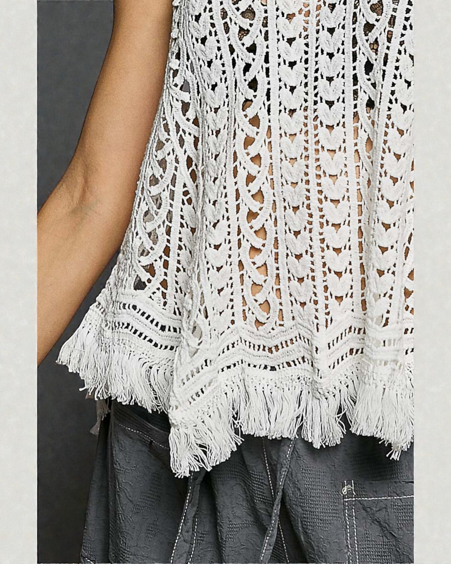White lace top with fringe details on a plain background