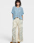 Woman wearing a blue floral top and cream pants with floral patterns on a white background