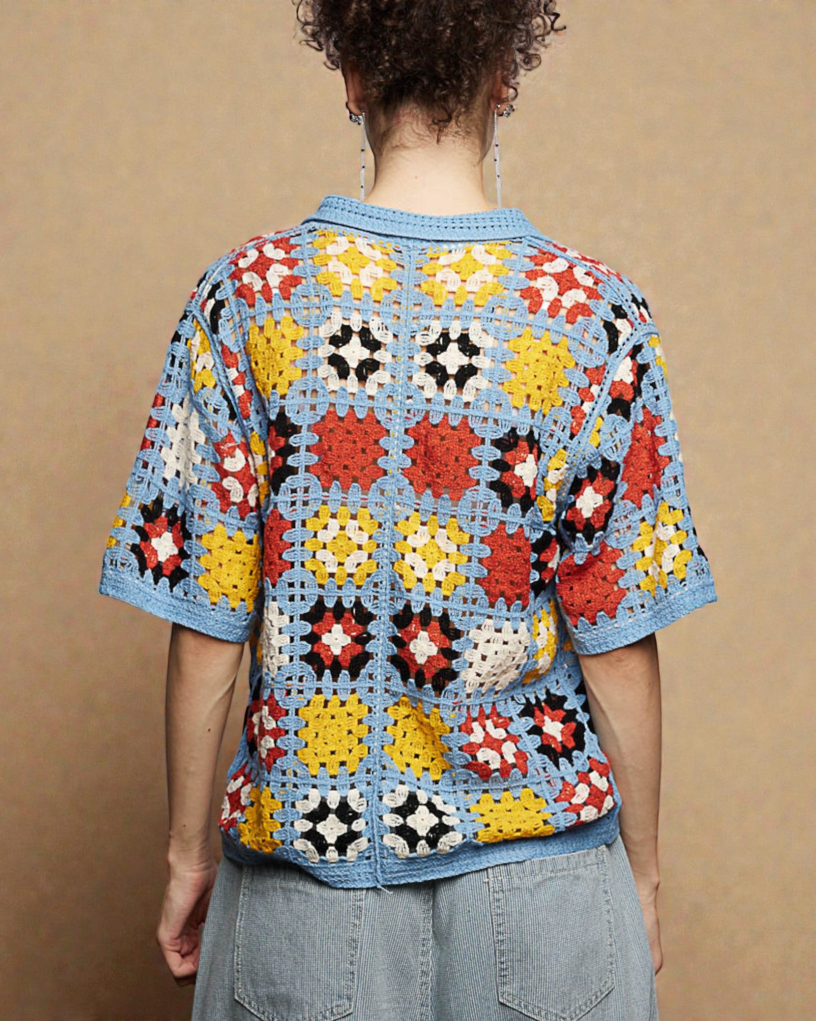 Person wearing a colorful crochet top against a beige background