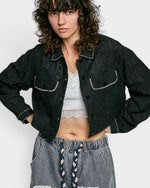 Person wearing a black denim jacket with white trim on a plain background