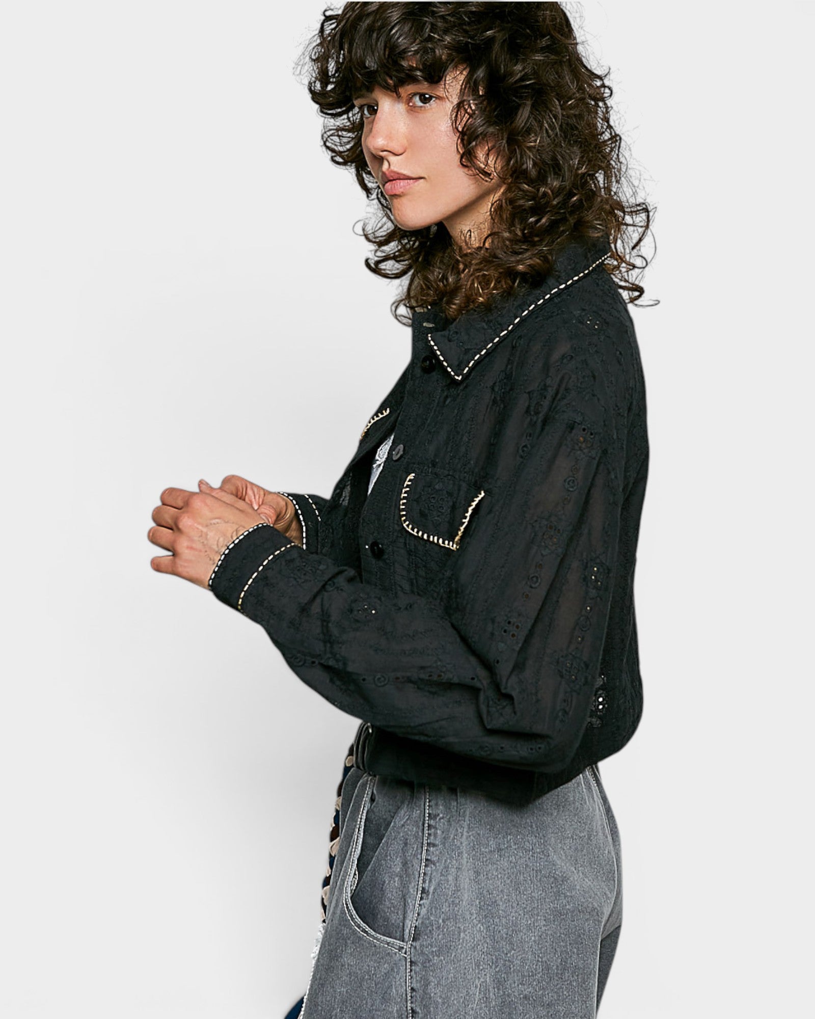 Person wearing a black embroidered jacket and gray jeans on a white background