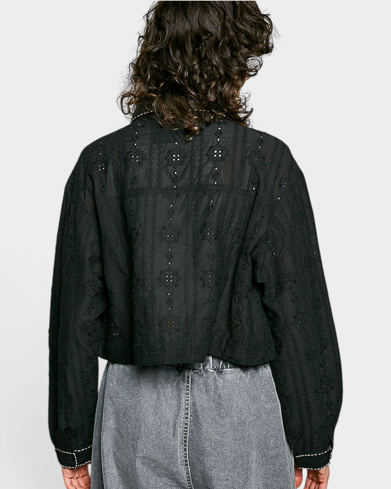 Person wearing a black embroidered blouse and gray pants on a white background