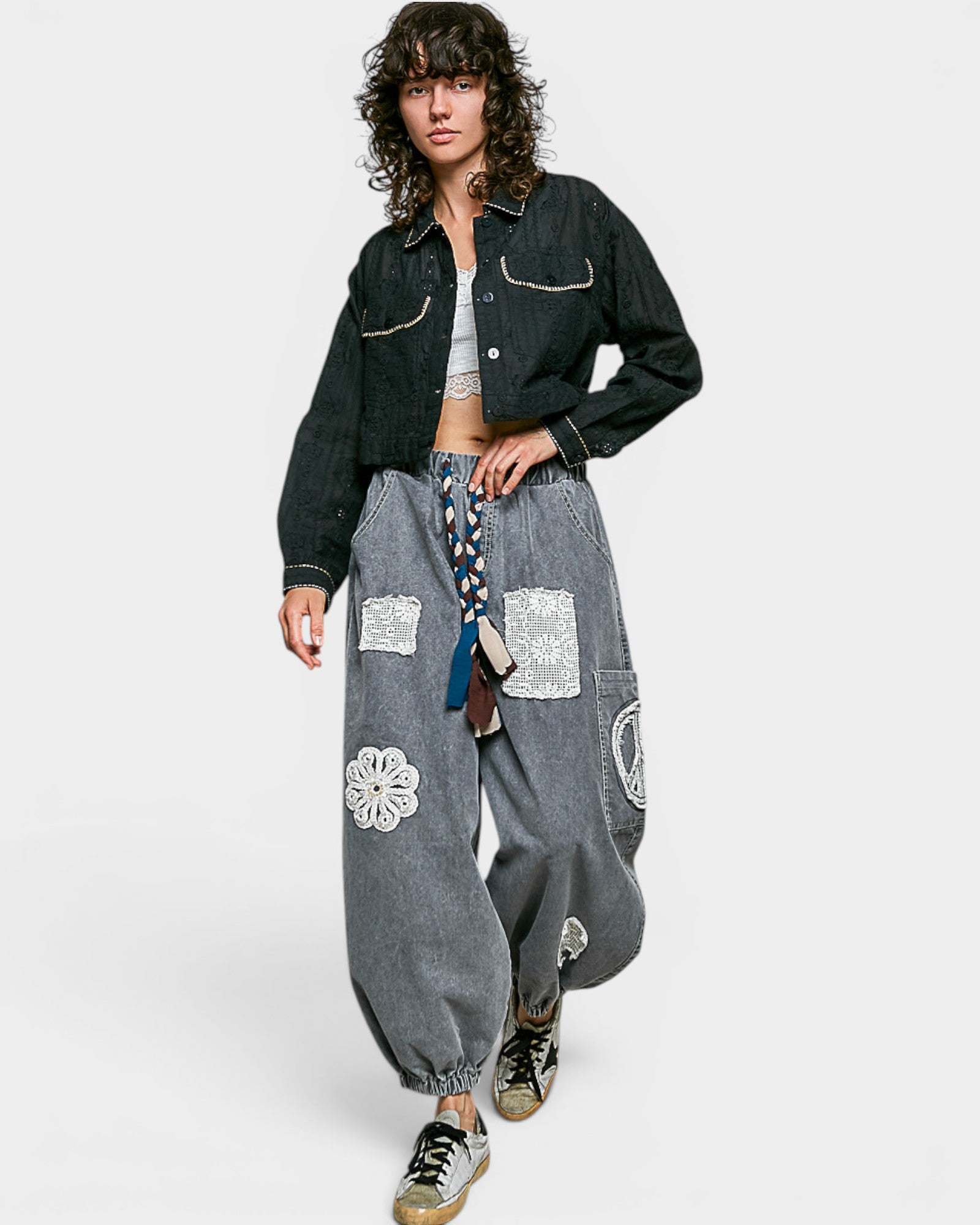 Person wearing a black denim jacket and gray baggy pants with floral patterns on a white background