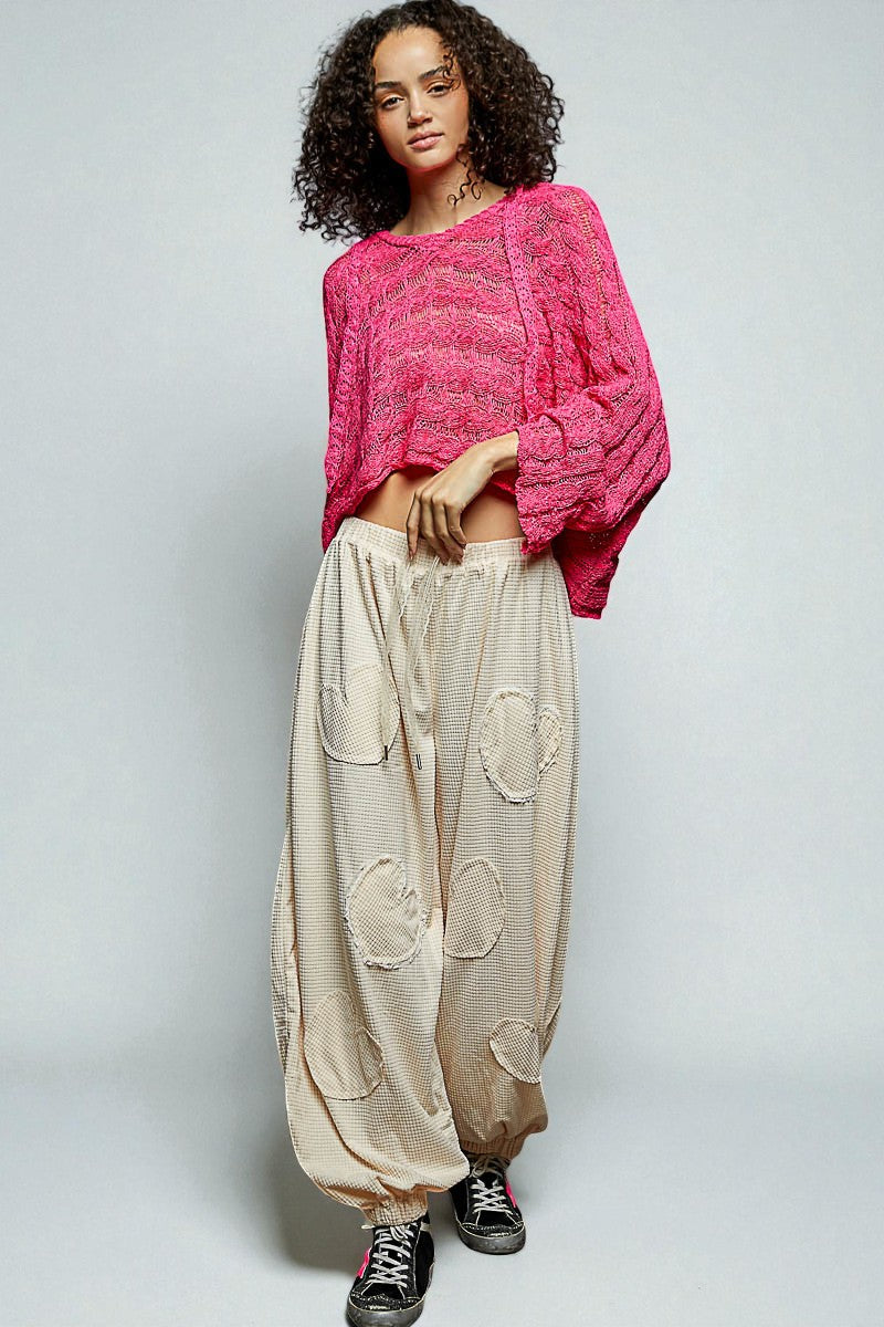 Woman wearing a pink sweater and beige pants with a white background