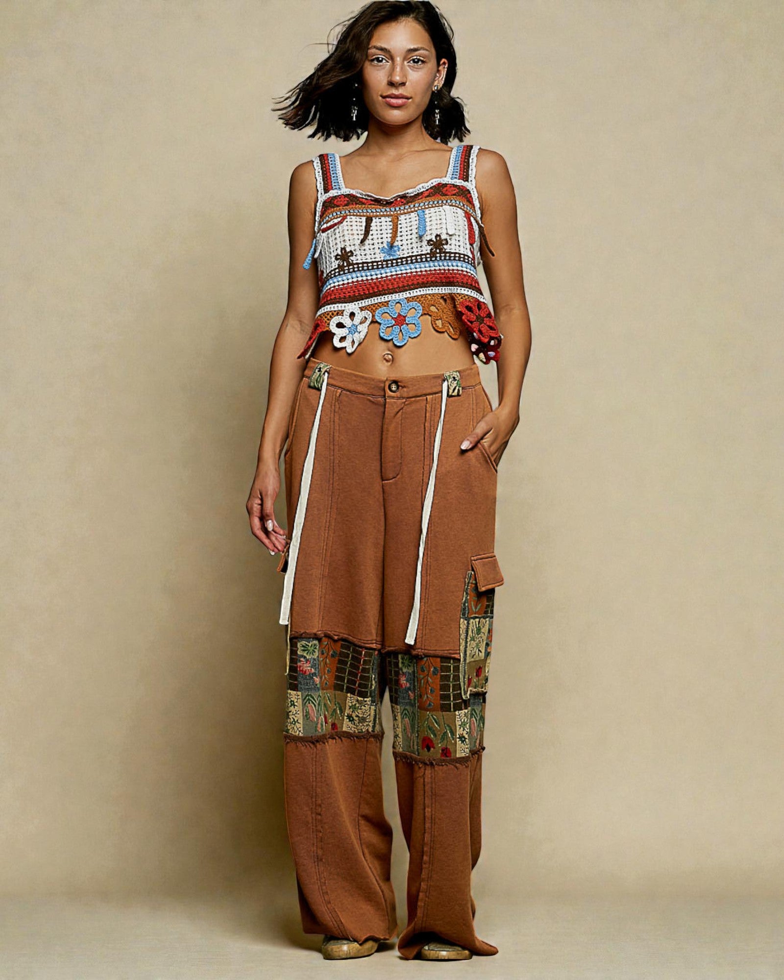 Woman wearing a colorful top and brown patchwork pants against a beige background