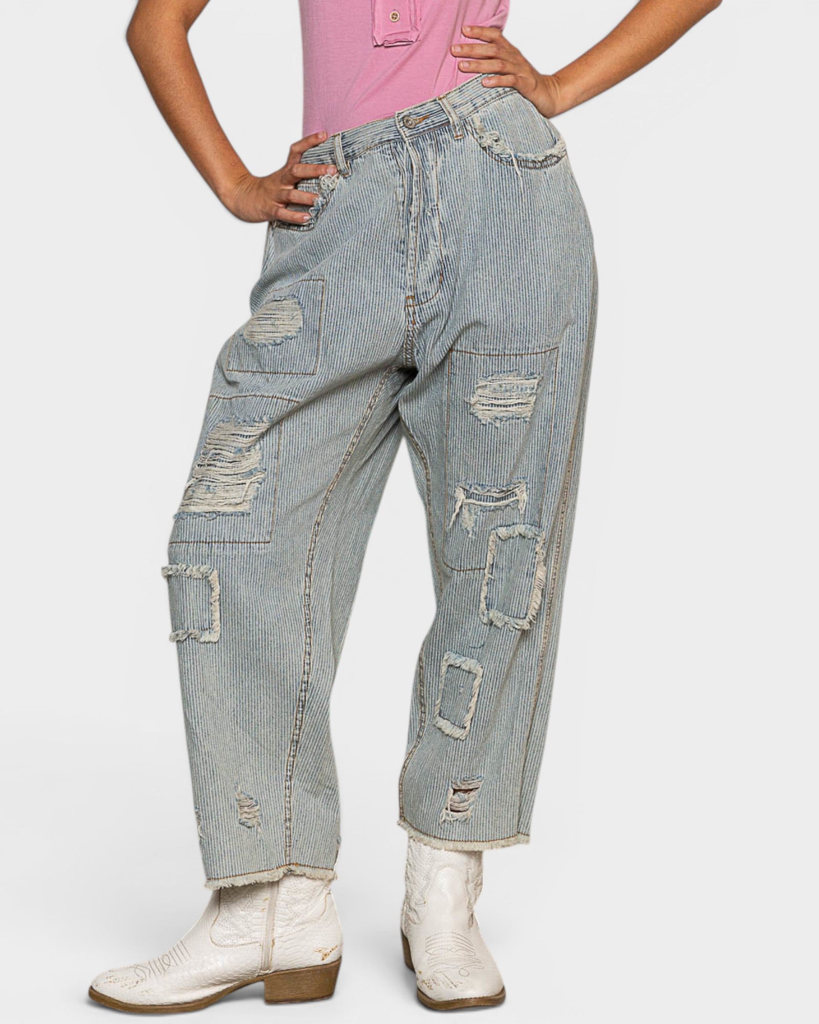 Person wearing ripped blue jeans and white boots on a light gray background