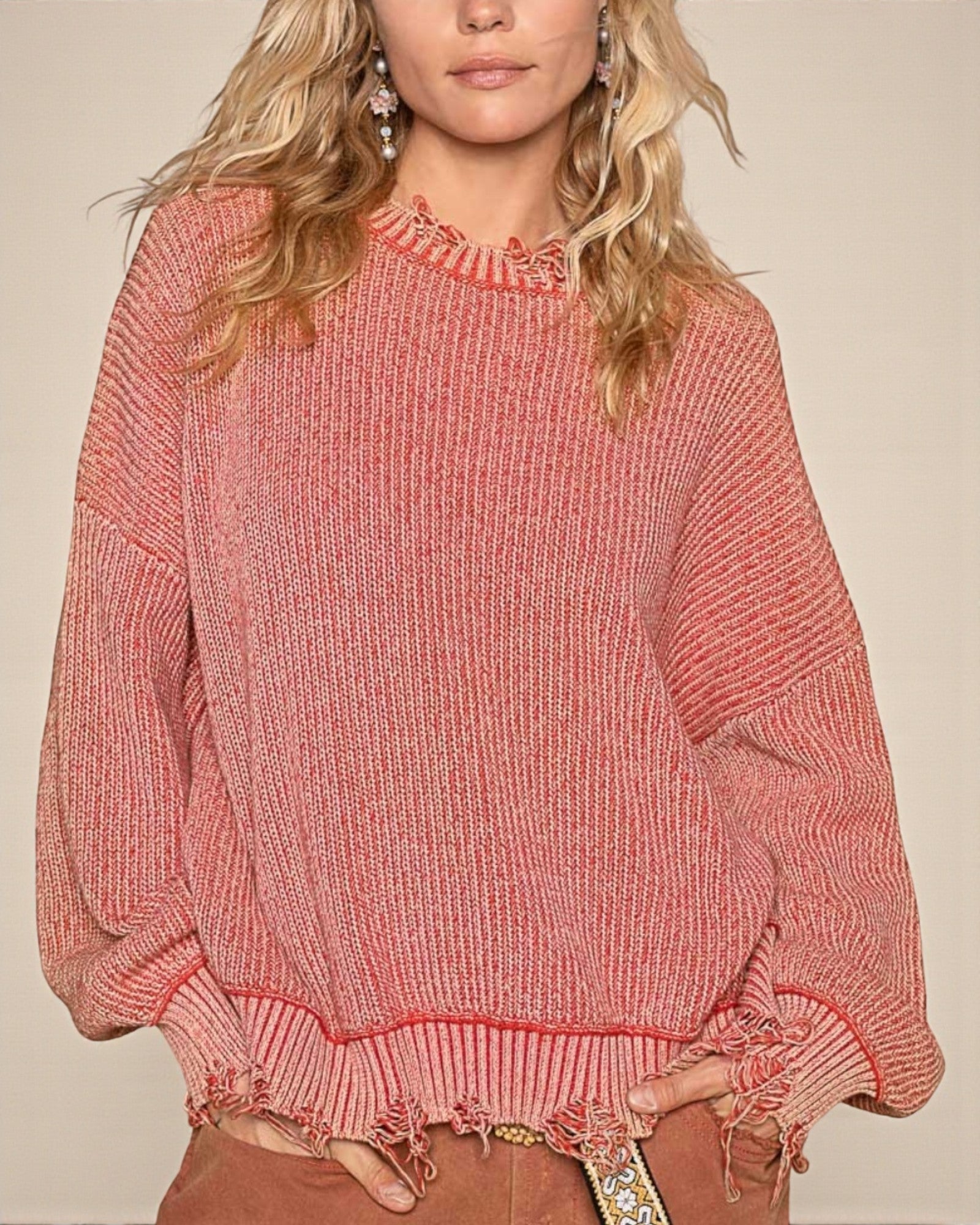 Person wearing a pink knitted sweater with fringe details on a beige background