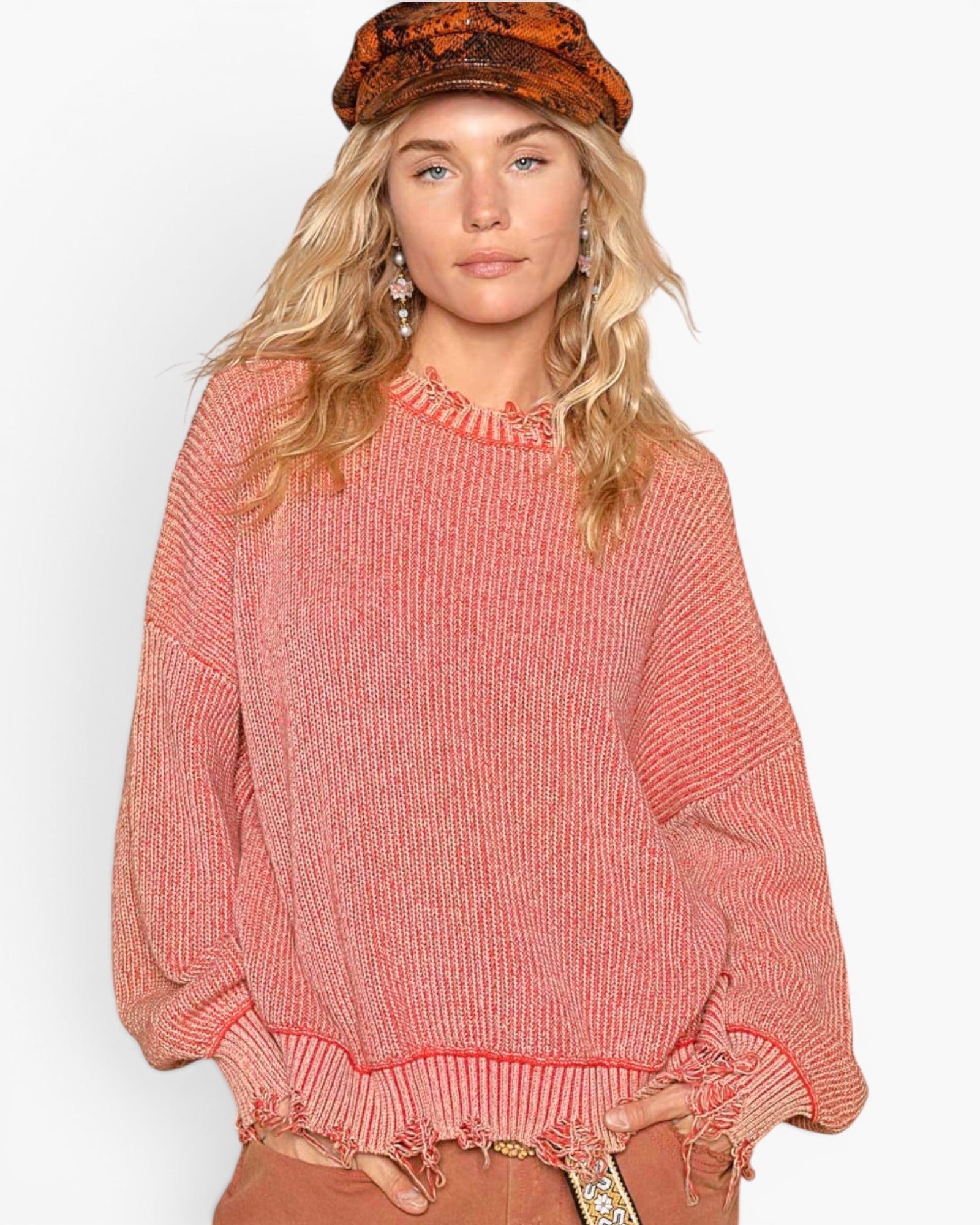 A woman wearing a coral pink ribbed knit sweater with a ruffled crew neck and distressed hem, paired with a brown patterned beret and brown pants, against a plain white background.