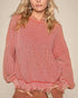 Person wearing a pink knitted sweater with fringe details on a beige background