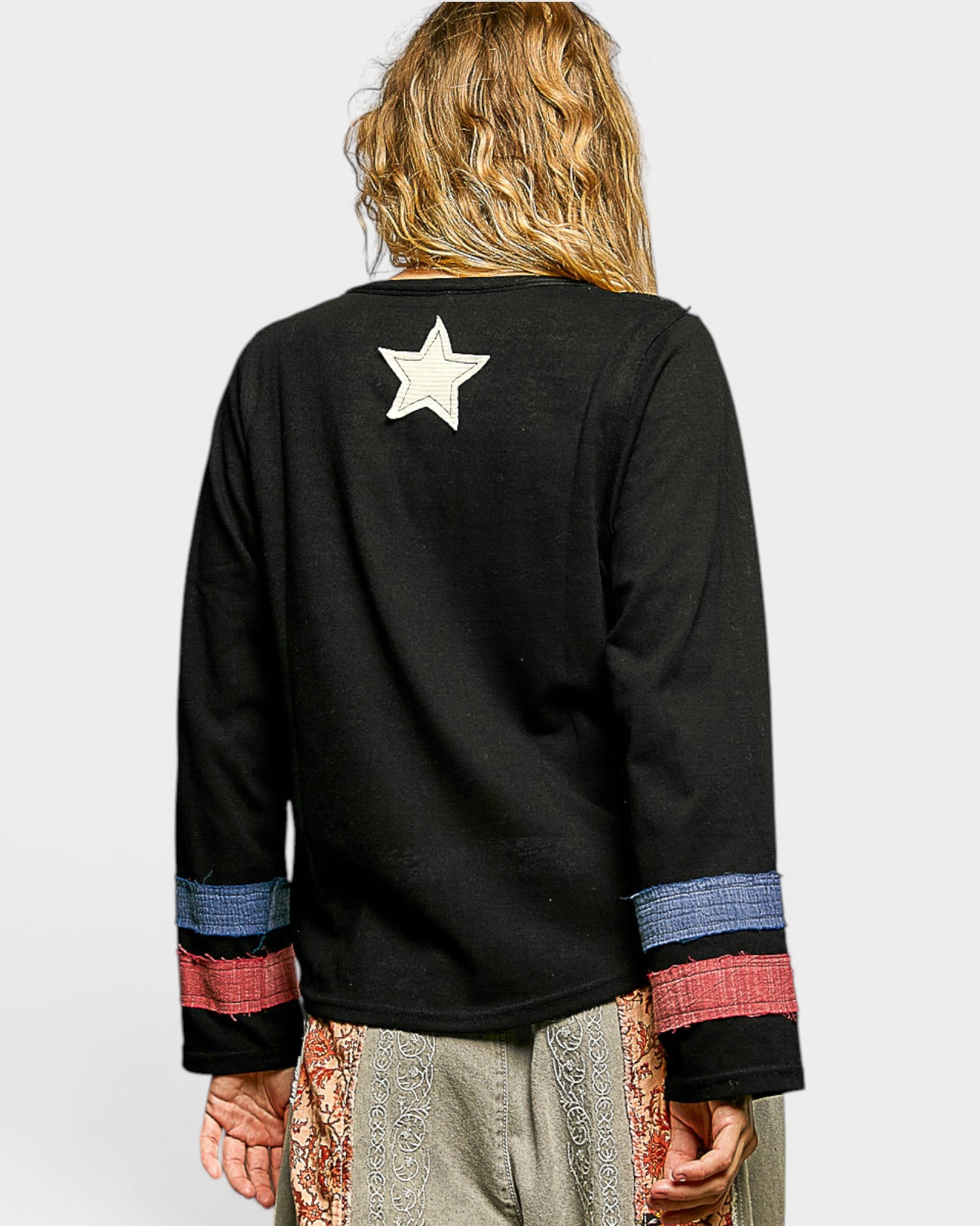 Person wearing a black long-sleeve shirt with colorful cuffs and a star on the back, standing against a light gray background.