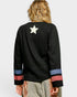 Person wearing a black long-sleeve shirt with colorful cuffs and a star on the back, standing against a light gray background.
