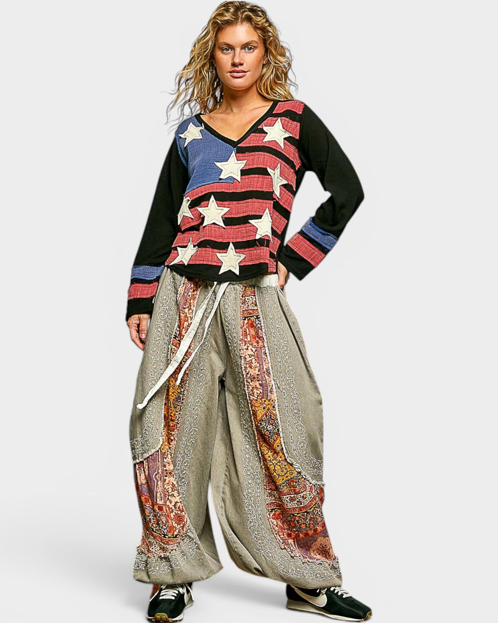 Woman wearing a colorful sweater with an American flag design and patterned pants on a white background