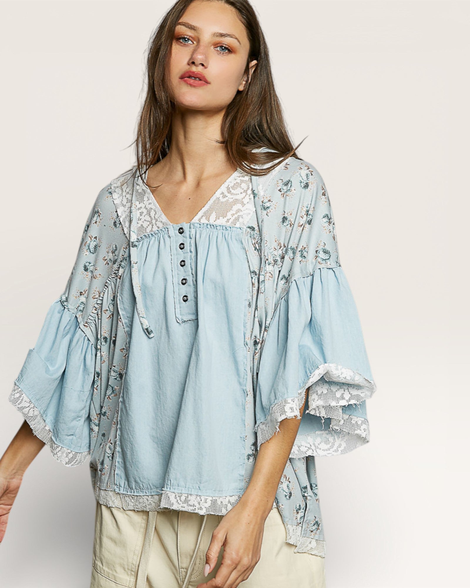 Woman wearing a light blue floral blouse with lace details on a plain background