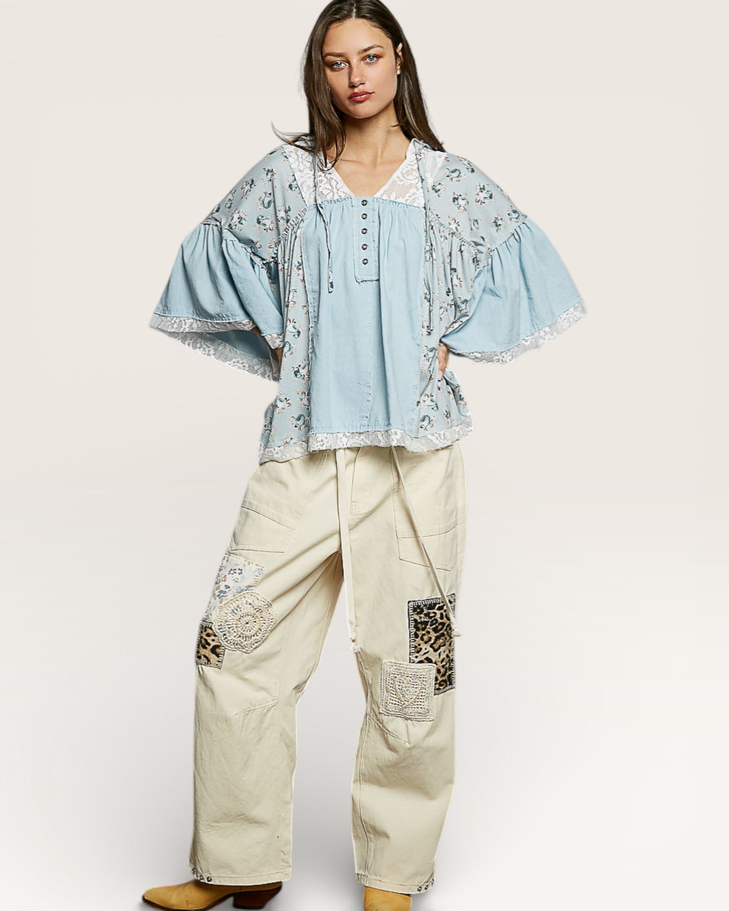 Woman wearing a light blue embroidered top and beige patchwork pants on a white background