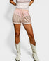 Person wearing a patterned top and shorts with white cowboy boots on a light gray background
