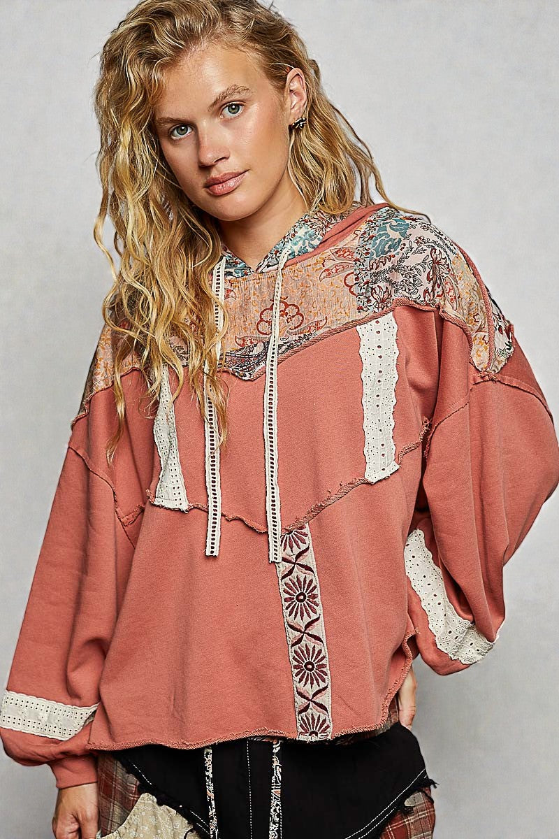 Woman wearing a patterned hoodie with lace details on a plain background