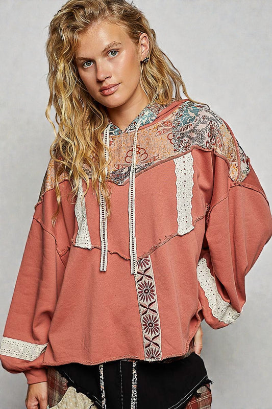 Woman wearing a patterned hoodie with lace details on a plain background