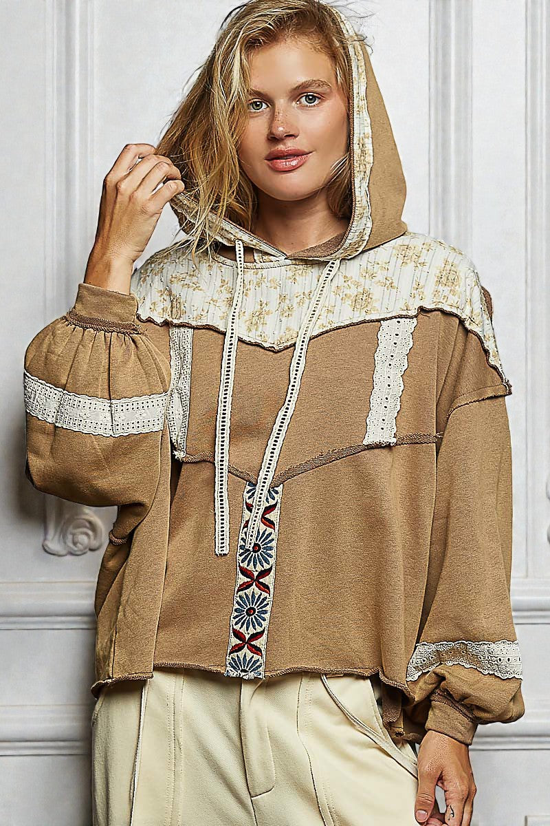 Woman wearing a brown hoodie with lace details against a white wall