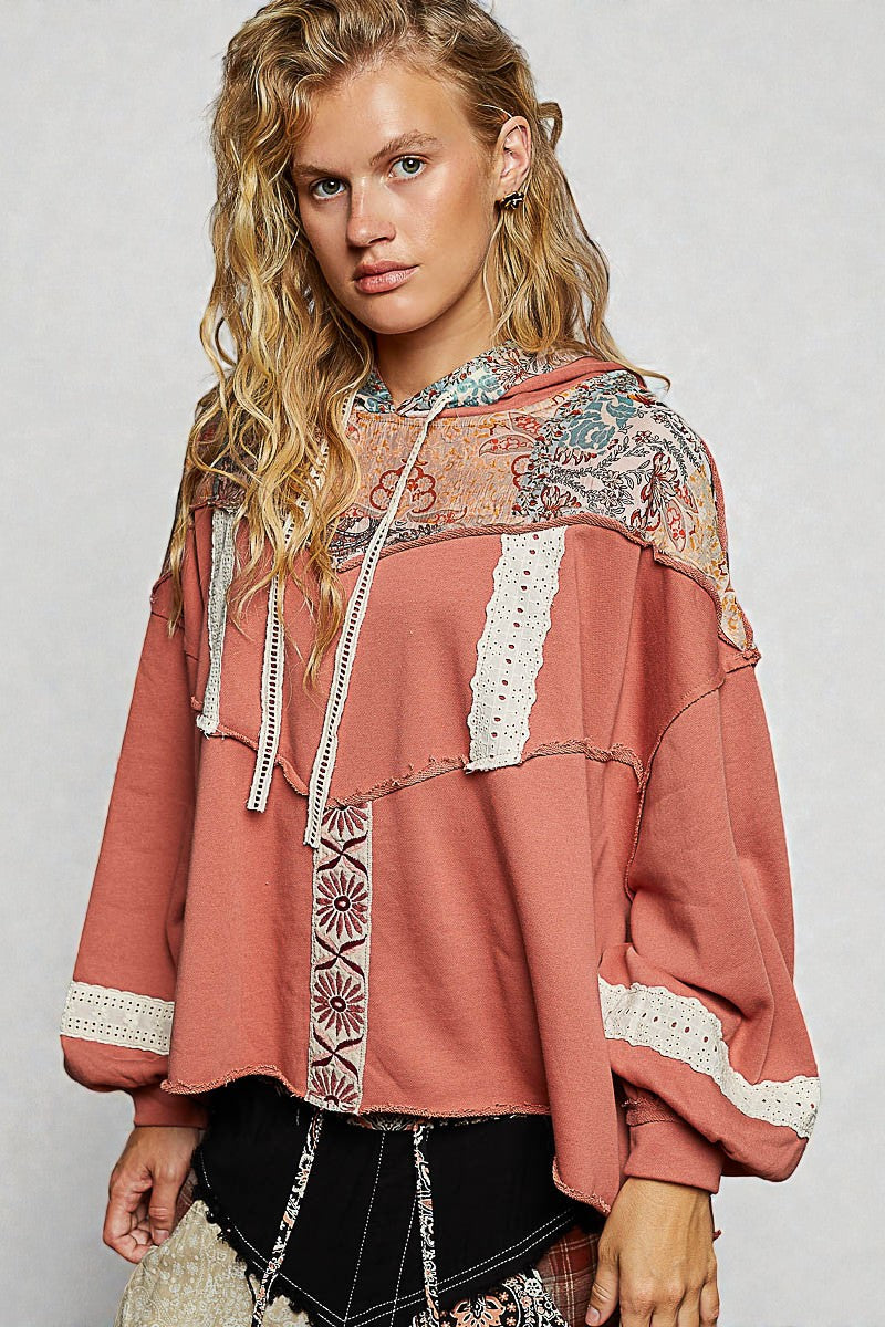 Woman wearing a pink hoodie with lace and patterned details on a plain background