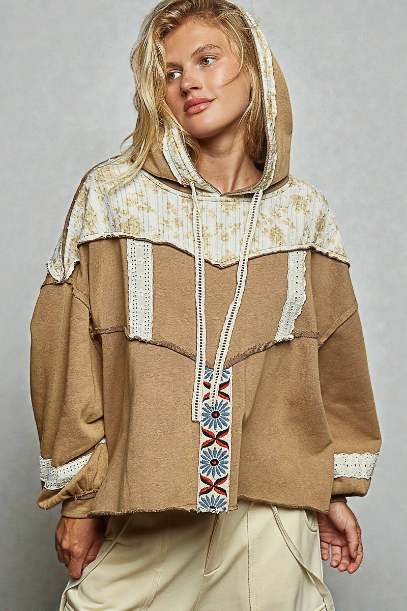 Woman wearing a brown hoodie with lace details on a gray background